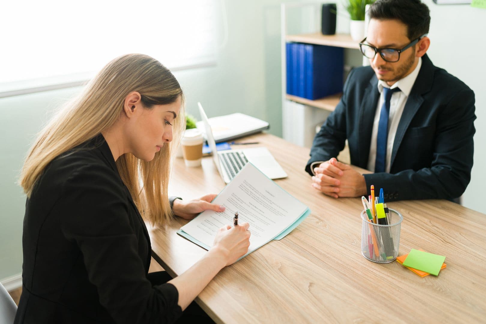 Client signing a contract or legal document across a desk from a professional lawyer in an office.